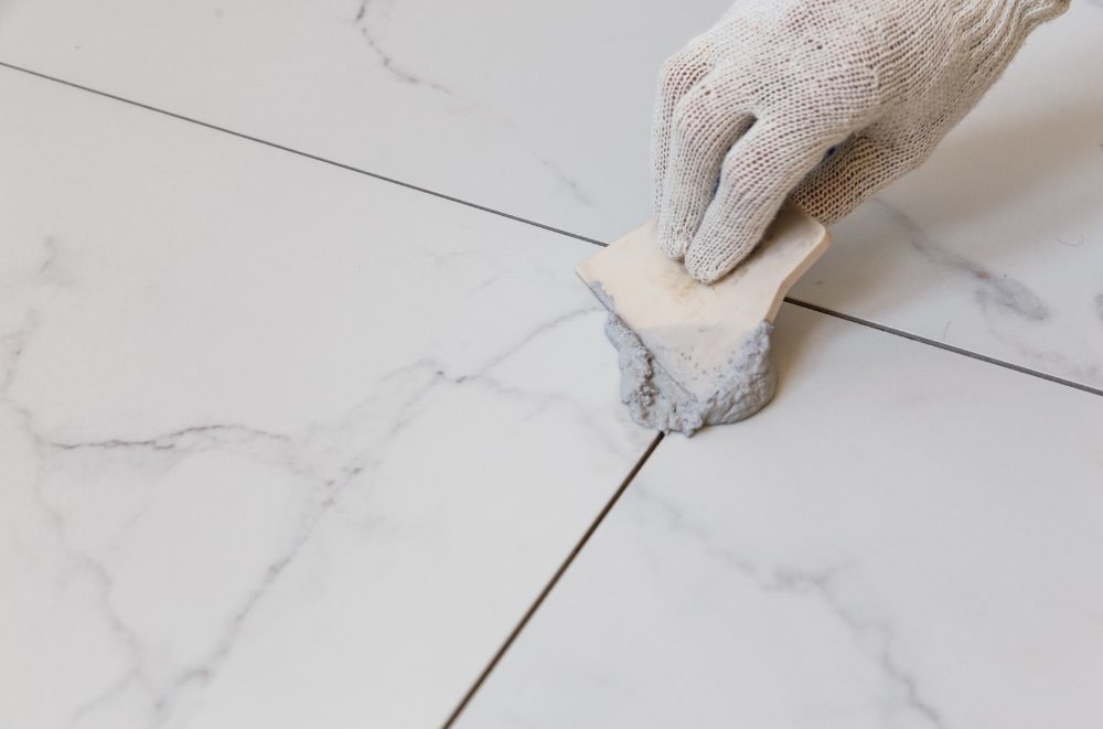 Grout sealing - person applying sealer to grout on white tiles